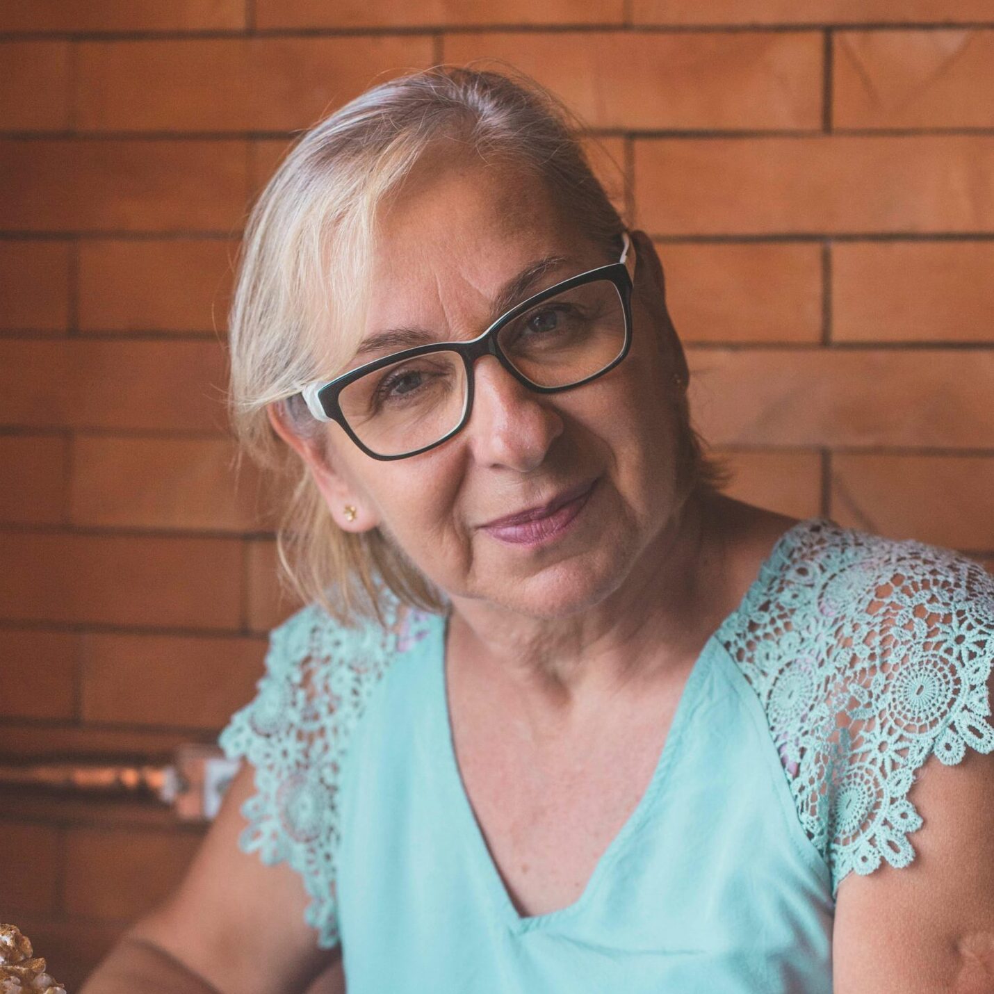 Elderly woman with eyeglasses smiling in a cafe holding a caramel latte.