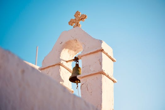 Close-up of a white Mykonos church bell tower under a clear blue sky.