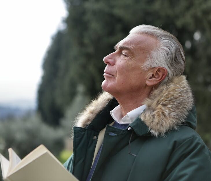 Senior man with white hair, eyes closed enjoying fresh air in Tuscany's natural setting.