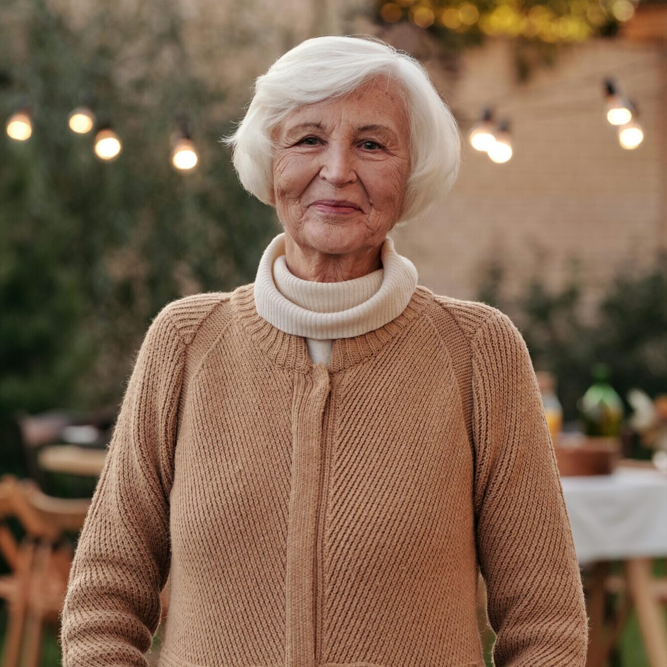 Cheerful senior woman in a cozy cardigan enjoying an outdoor gathering in the garden.